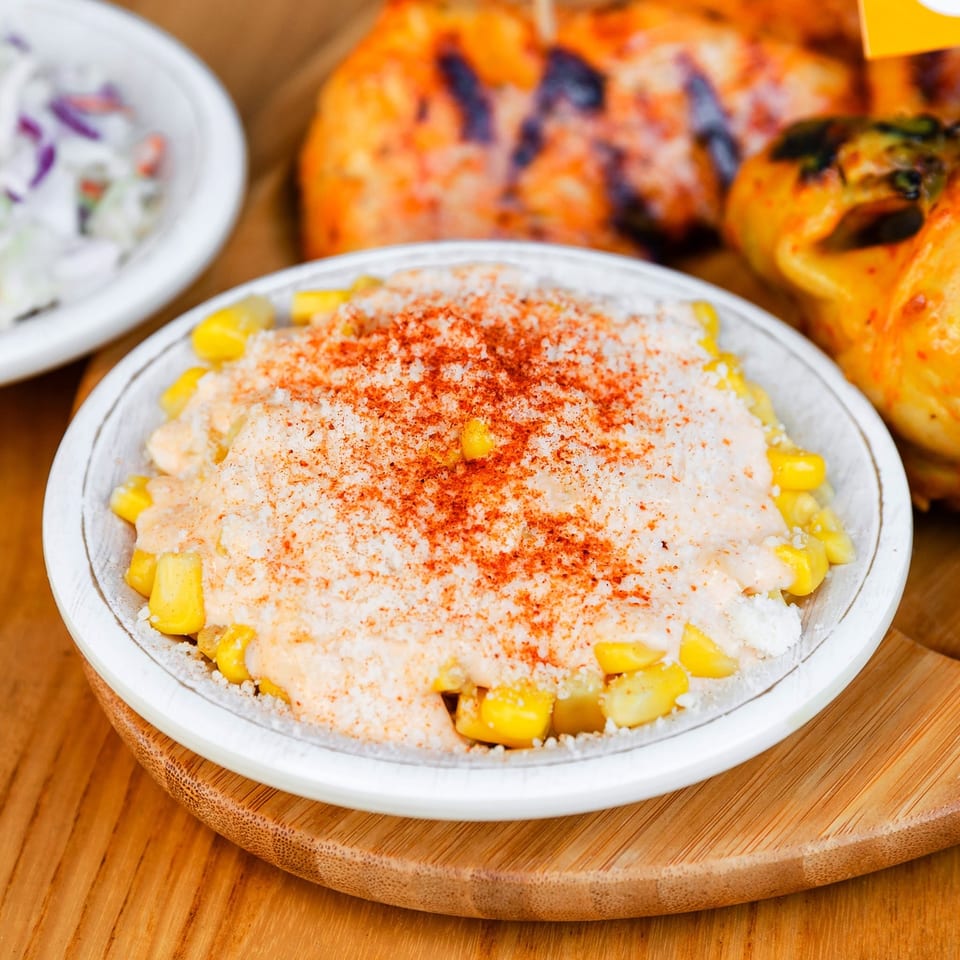 Creamy elote in a white bowl, topped with white cheese and red chili powder.
