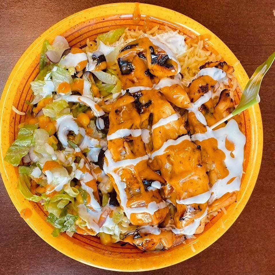 Grilled chicken and rice bowl with lettuce, white, and orange sauces on a yellow plate.