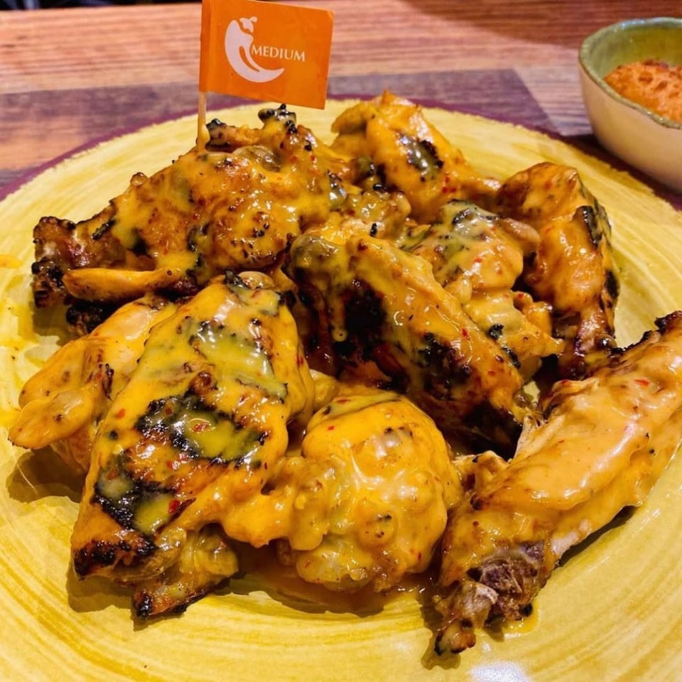 Grilled chicken wings covered in creamy yellow sauce on a yellow plate, with a "Medium" spice flag.