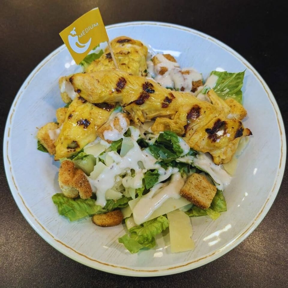 Grilled chicken Caesar salad with croutons, cheese, dressing, and a "medium" spice flag.