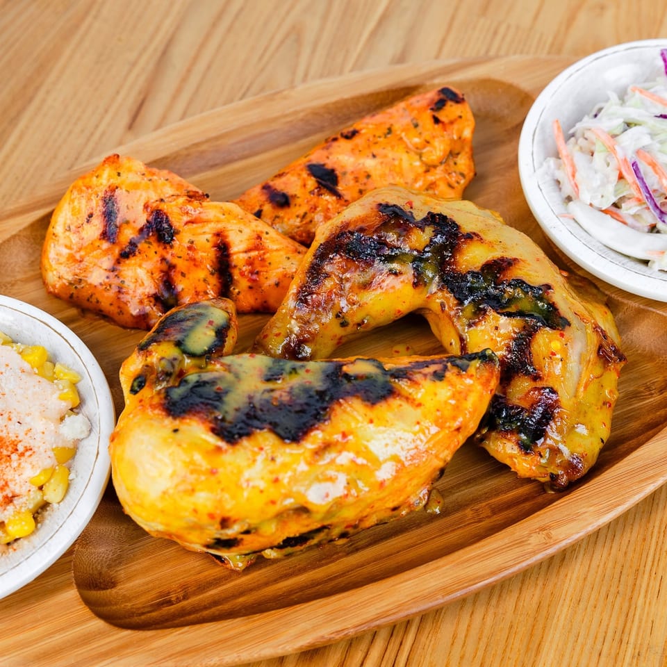 Assorted grilled chicken pieces with coleslaw and corn on a wooden tray.