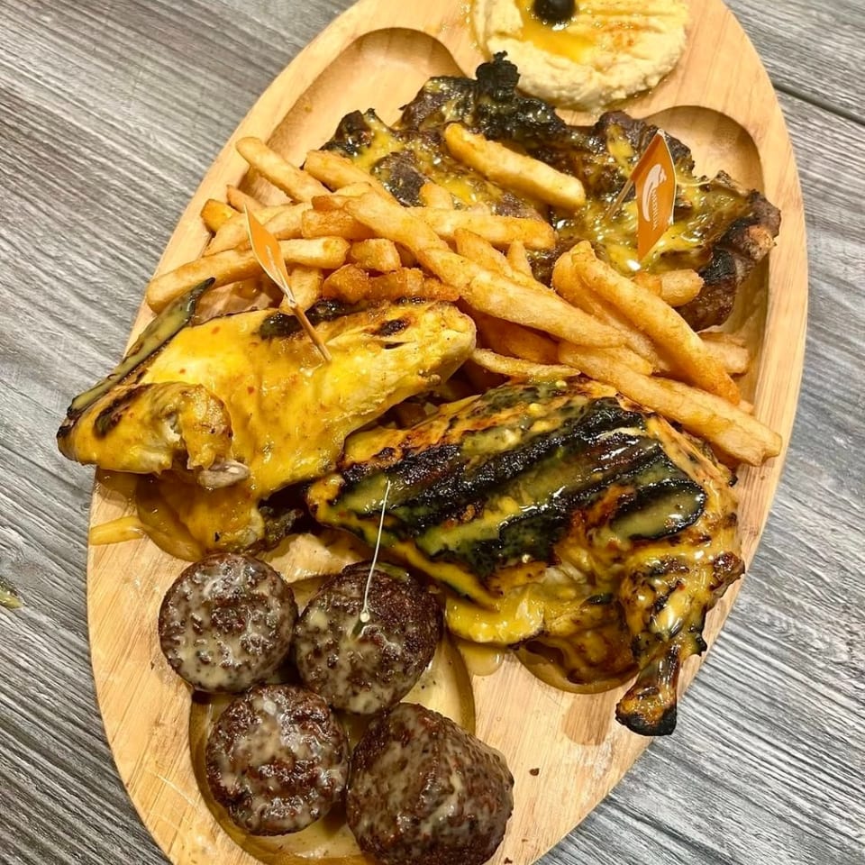 Grilled chicken, golden fries, saucy meatballs, and hummus on a wooden serving platter.