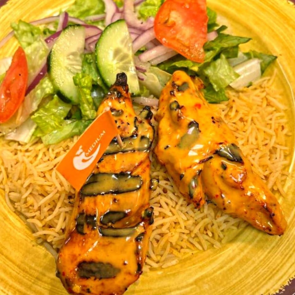 Two grilled chicken pieces with yellow sauce, rice, and salad, one with a "MEDIUM" flag.