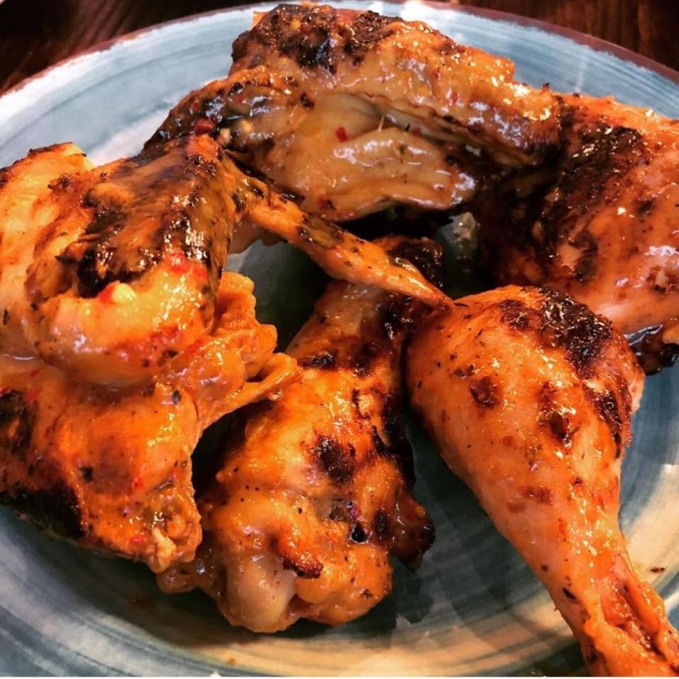 Juicy grilled chicken wings and drumsticks with charred skin served on a blue plate.
