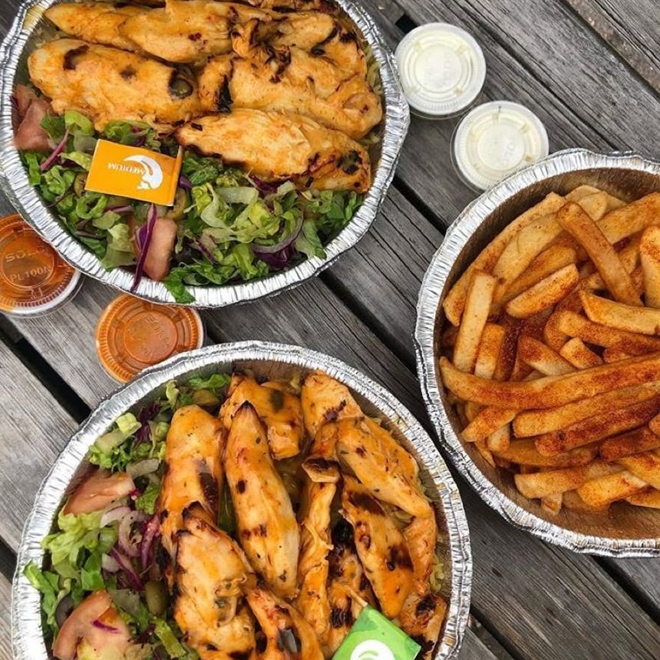 Two grilled chicken and salad meals with seasoned fries and sauces on a wooden table.